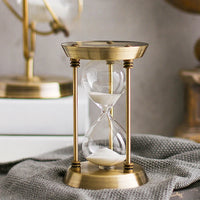Goldfarbene IRONFORM Sanduhr mit weißem Sand auf grauem Textil.
